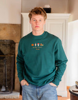 Cosy Autumn embroidered unisex sweatshirt in Deep Green worn by a model, with a pumpkin, owl, toadstool and snail design